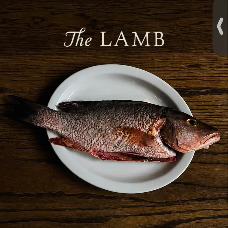 Pescado entero servido sobre plato blanco en mesa de madera, The Lamb