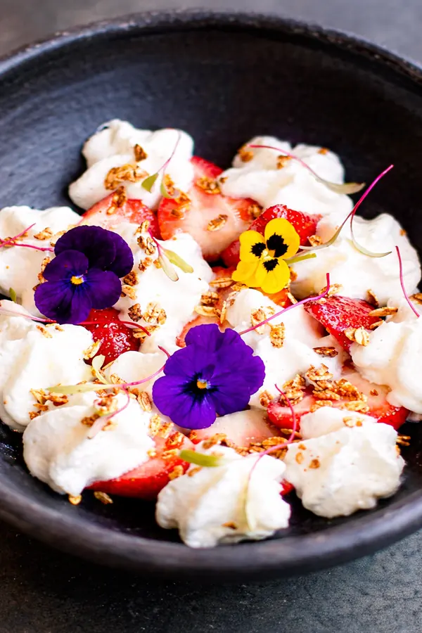Burrata con fresas y flores comestibles en plato oscuro