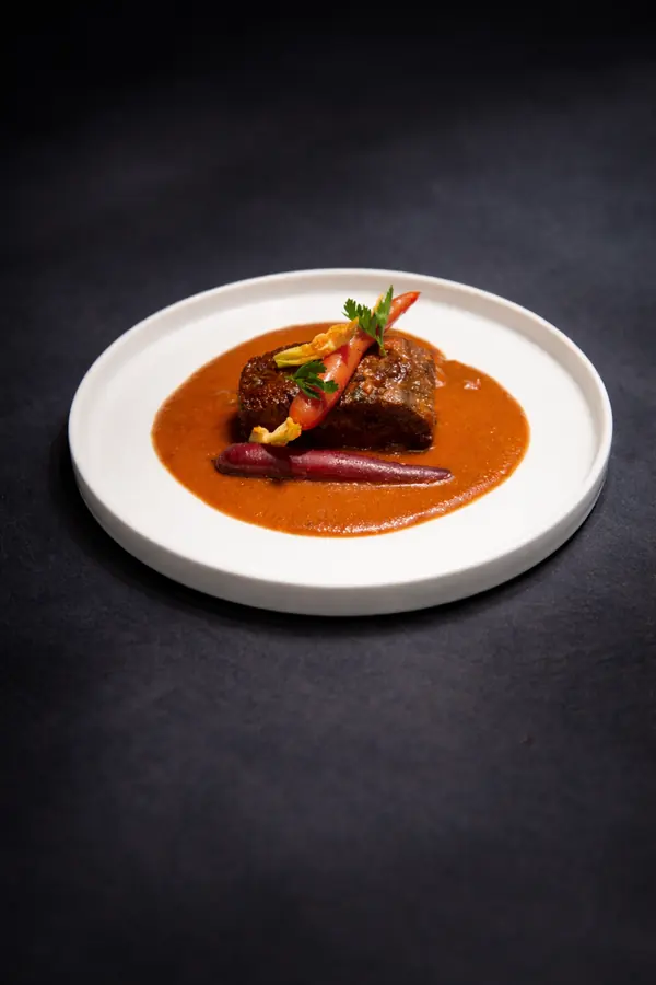 Corte de carne en salsa roja sobre plato blanco