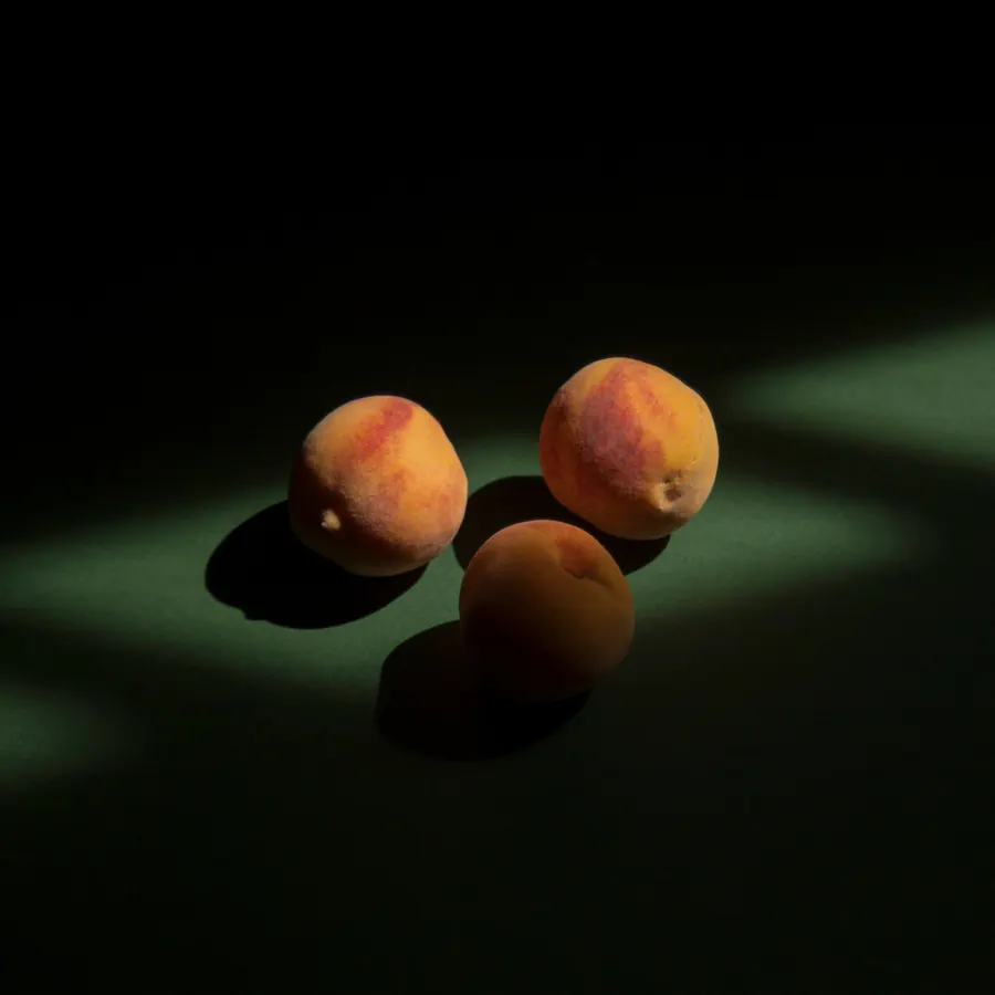 Tres duraznos bajo un haz de luz sobre fondo verde oscuro