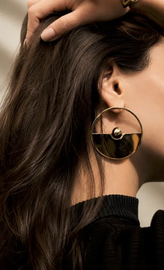 Arete dorado circular sobre cabello oscuro